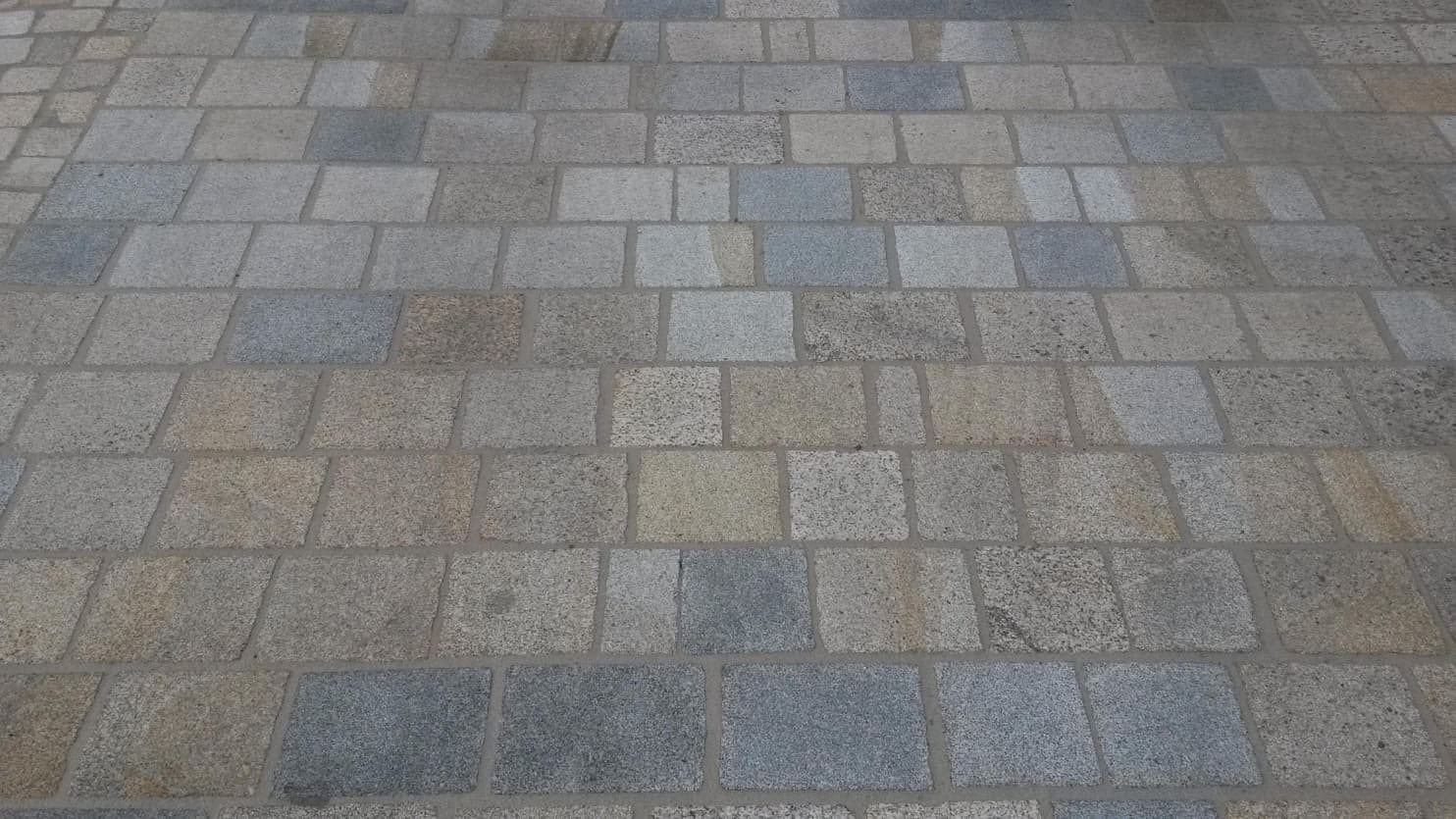 Dlažba z formátovaných žulových desek v různých odstínech, vytvářející odolný a estetický povrch.