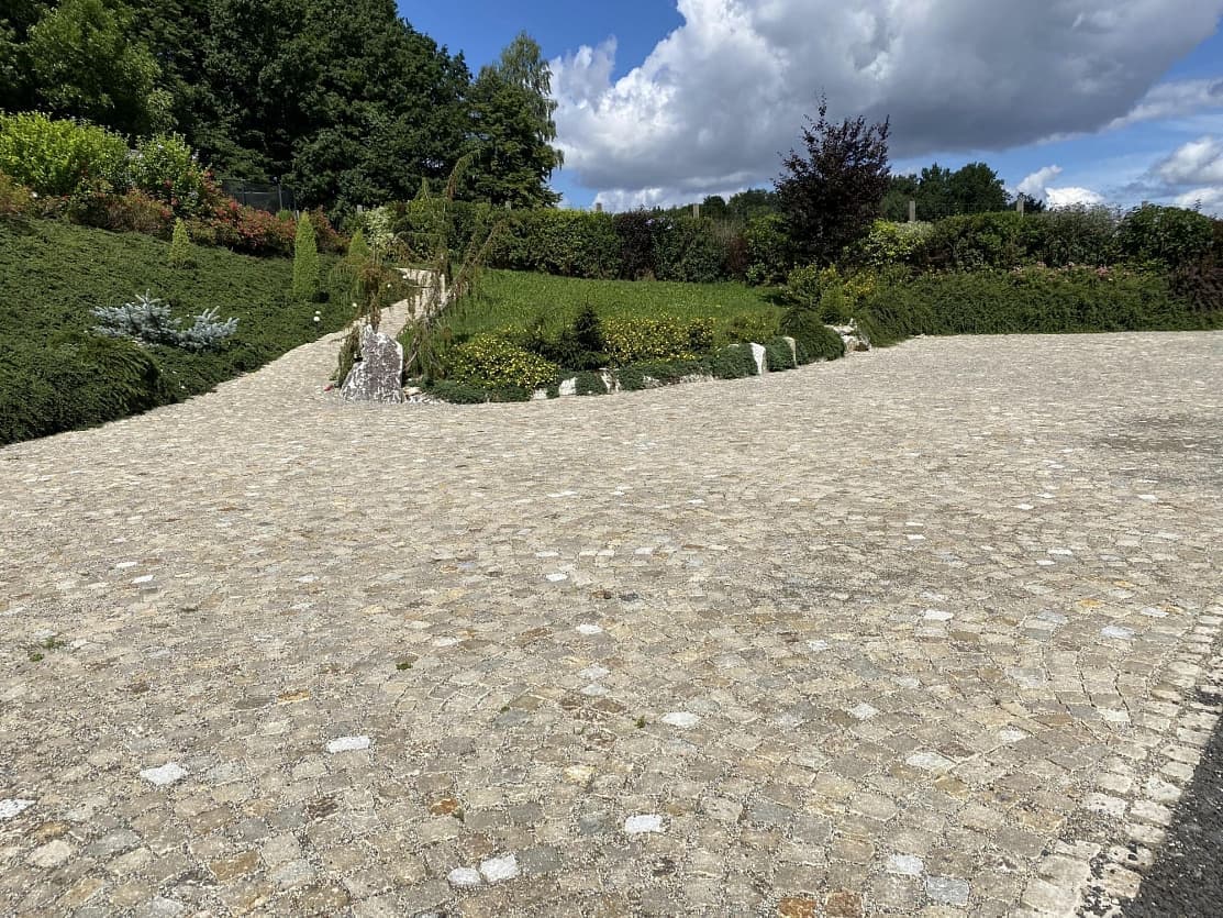 Rozlehlá plocha vydlážděná šedožlutými žulovými kostkami elegantně propojuje příjezdovou cestu se zahradou.