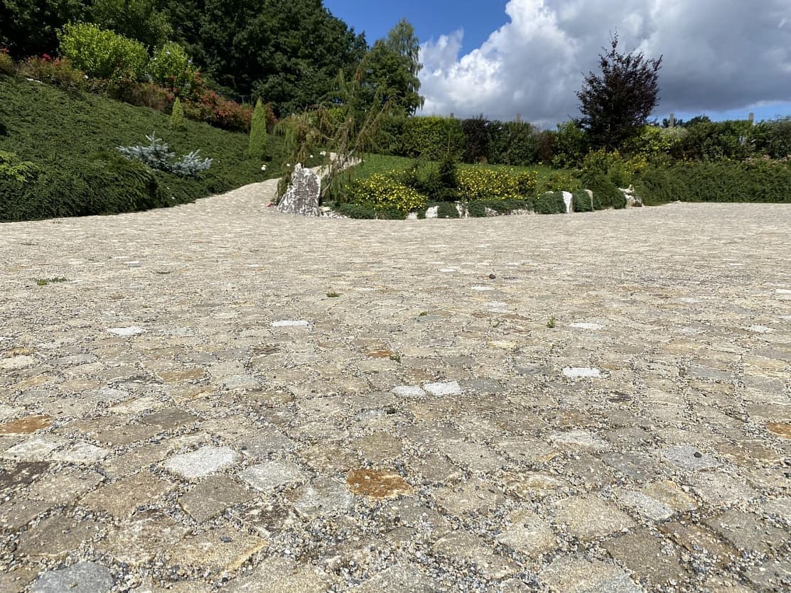 Detailní pohled na šedožluté žulové kostky, které tvoří pevnou a estetickou dlažbu ladící s okolní zahradní úpravou.