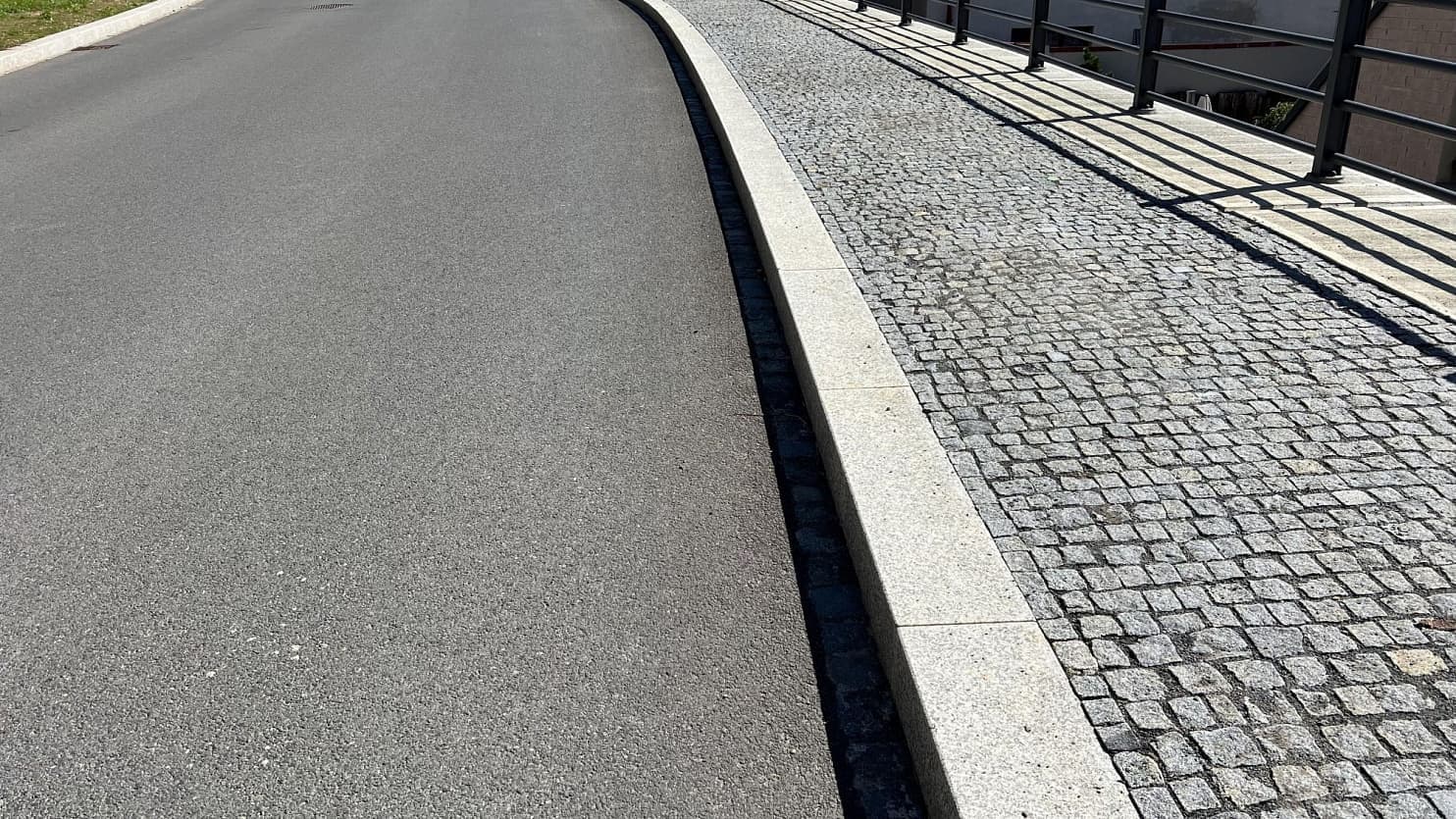 Chodník ze šedých žulových kostek, lemovaný řezaným obrubníkem, elegantně navazuje na asfaltovou vozovku.