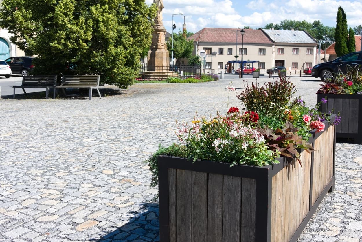 Povrch náměstí ze žulových kostek v šedožlutém odstínu, doplněný květinovými truhlíky, vytváří estetický veřejný prostor.