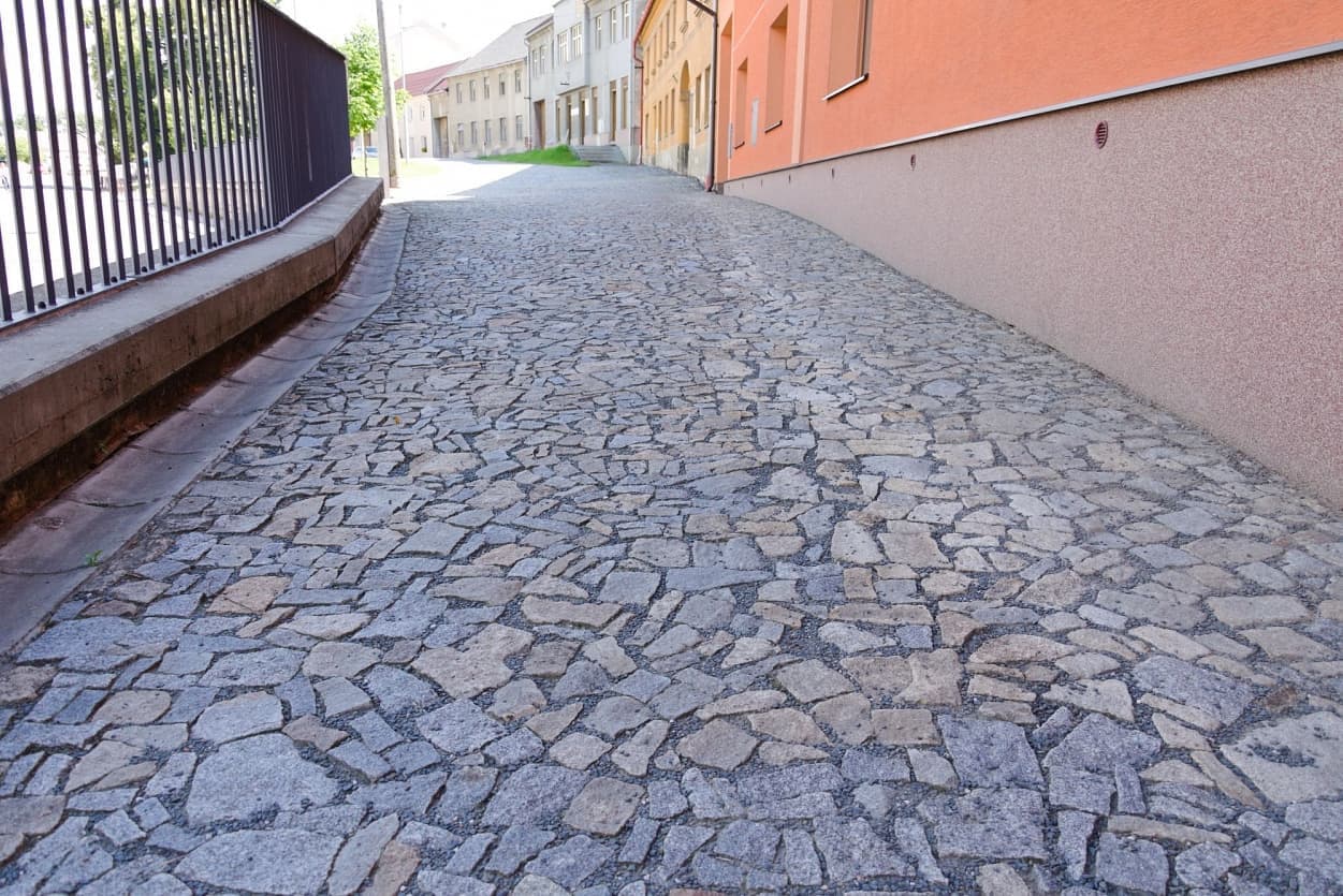 Povrch dlážděný žulovými odštěpky v šedožlutém odstínu dodává ulici autentický vzhled a zároveň zajišťuje její životnost.