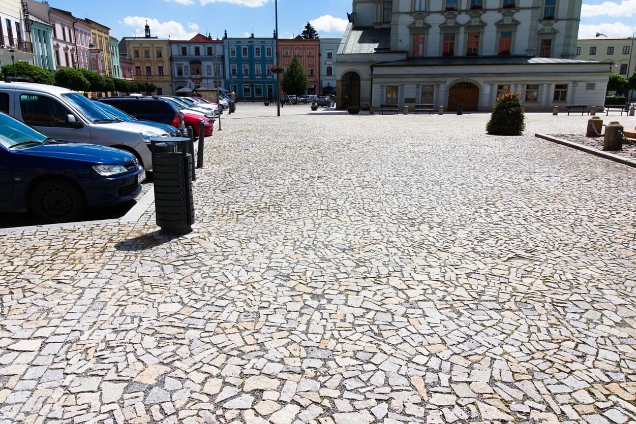 Parkoviště na uničovském náměstí, pokryté žulovými odseky ve šedožlutém odstínu, s historickými domy v pozadí.