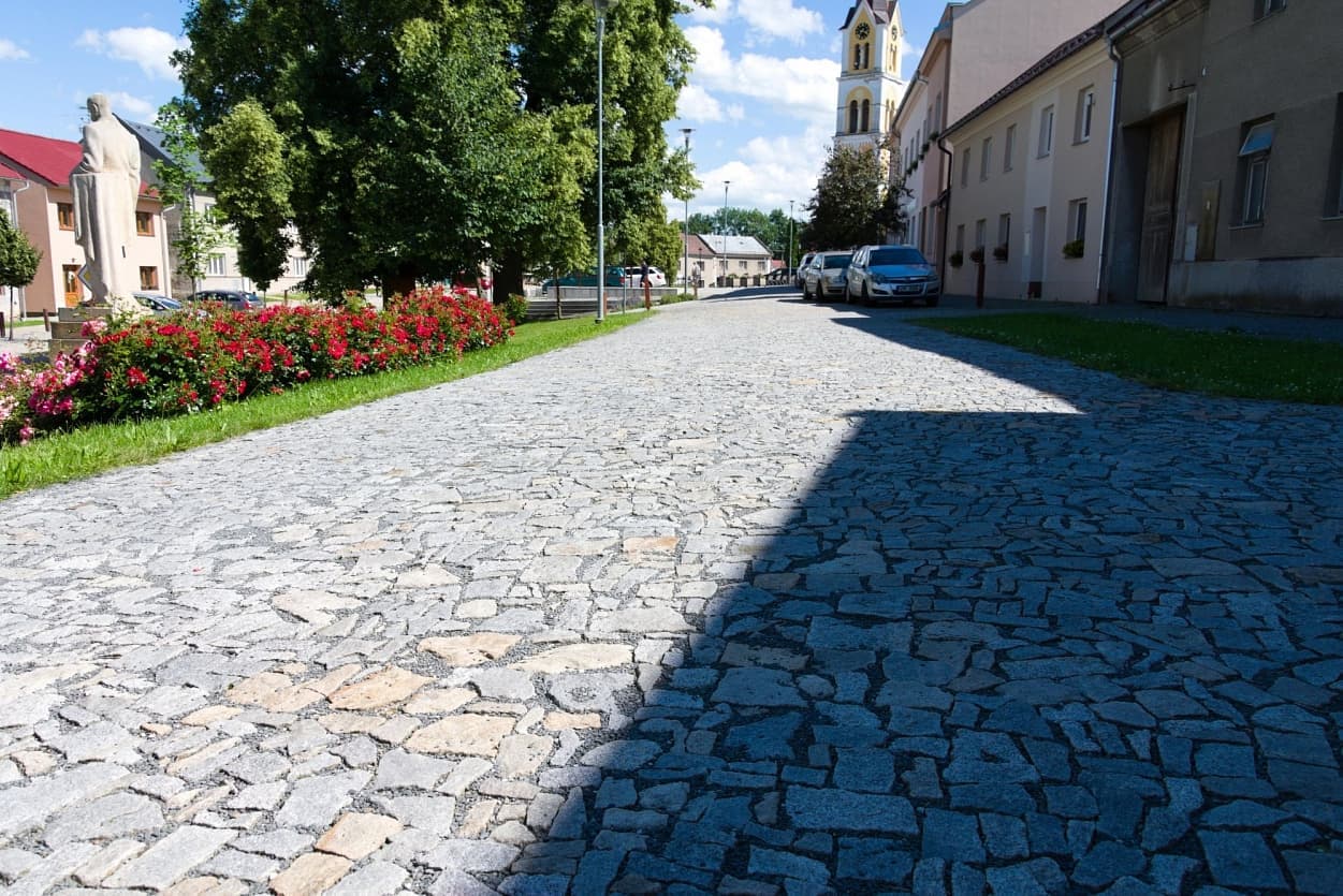 Cesta vydlážděná žulovými odseky v šedožlutém odstínu vytváří odolný a vizuálně atraktivní povrch v harmonii s prostředím.