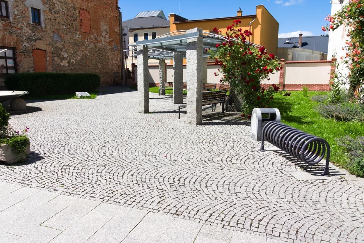 Obdélníkový přístřešek na žulových sloupech, vějířová žulová dlažba a spirálový stojan na kola v městském prostoru.