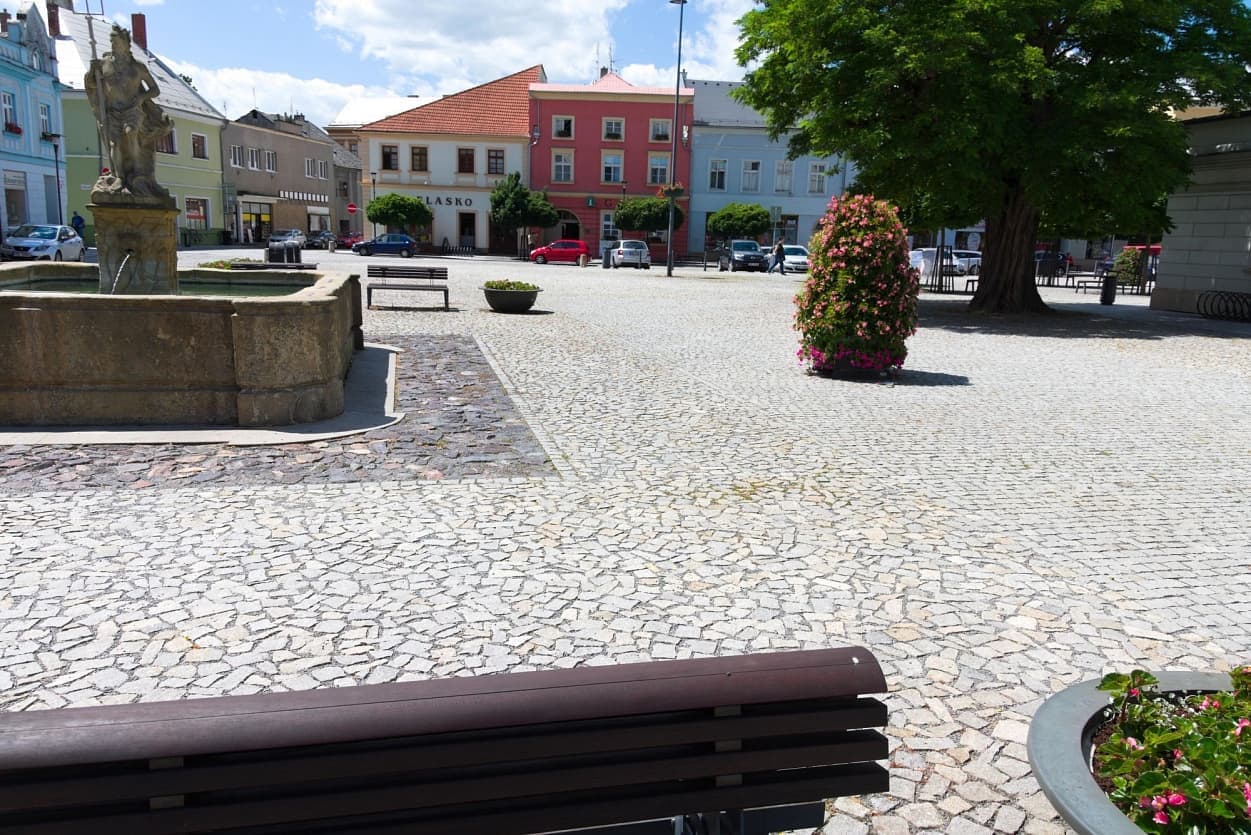 Historická kašna v Uničově s tříděnými žulovými odseky a květinovou výzdobou na dlážděném náměstí.