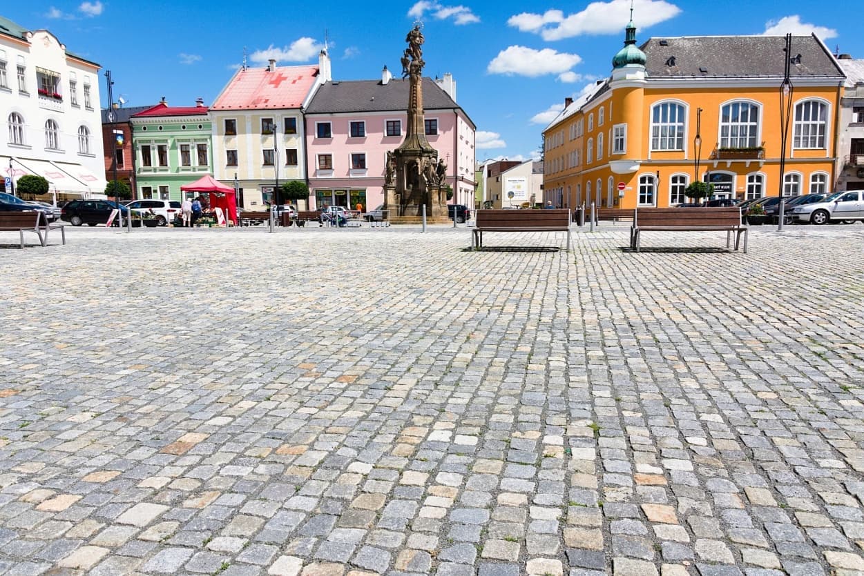 Náměstí v Litovli s žulovou dlažbou z různobarevných kostek, lavičkami, historickou sochou a barevnými domy v pozadí.