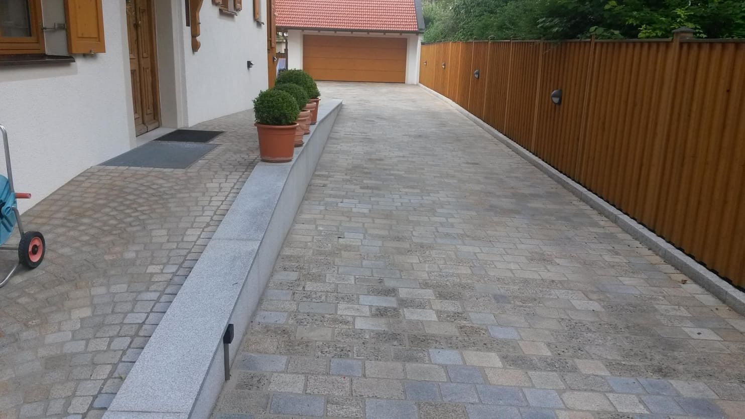 Příjezdová cesta s formátovanou žulovou dlažbou, obloženou zídkou a elegantním vstupem do domu s obloukovou dlažbou.