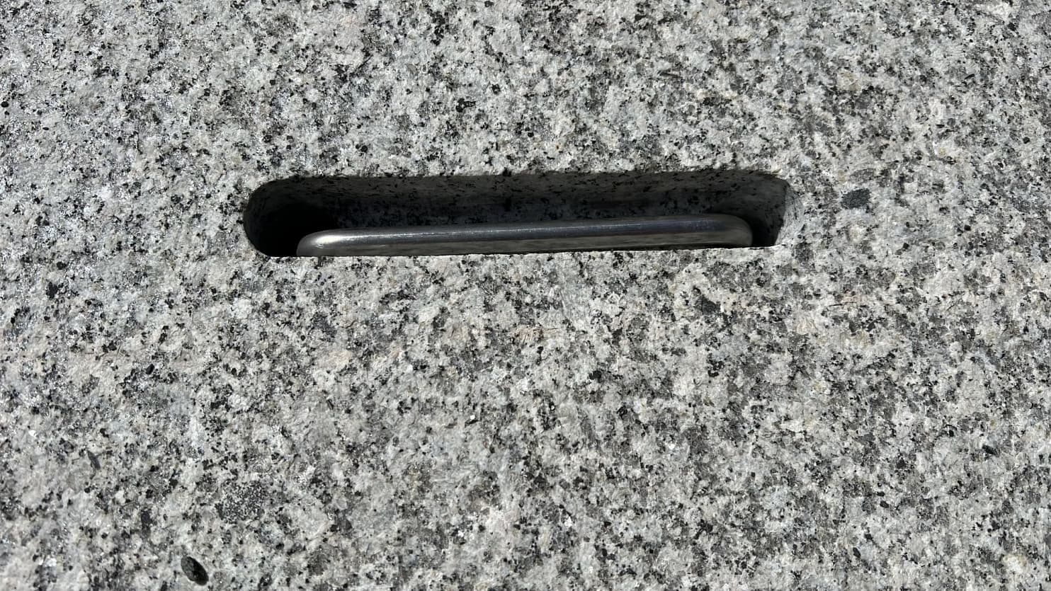 Detail hrubozrnné žuly s vyfrézovaným otvorem a kovovým madlem, ukazující strukturu přírodního kamene a precizní zpracování. 