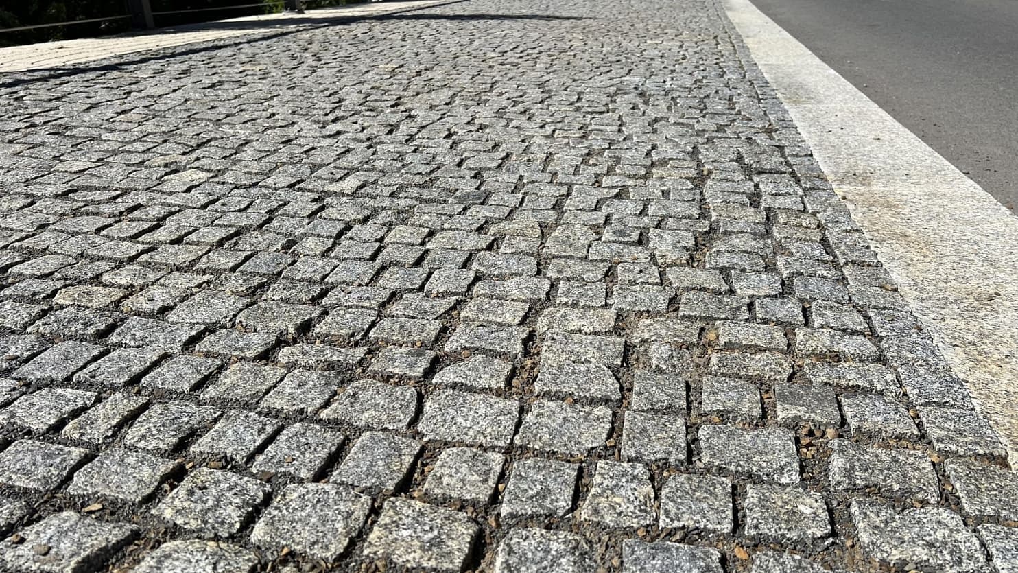 Detailní pohled na chodník z žulových kostek v šedém odstínu, precizně osazených vedle řezaného obrubníku pro odolnost a estetický vzhled.