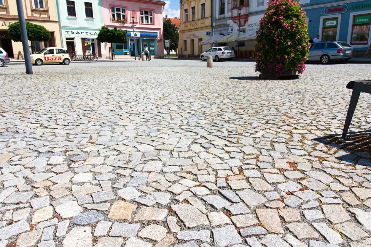 Dlažba z odštěpků žuly na historickém náměstí s barevnými fasádami domů v pozadí.