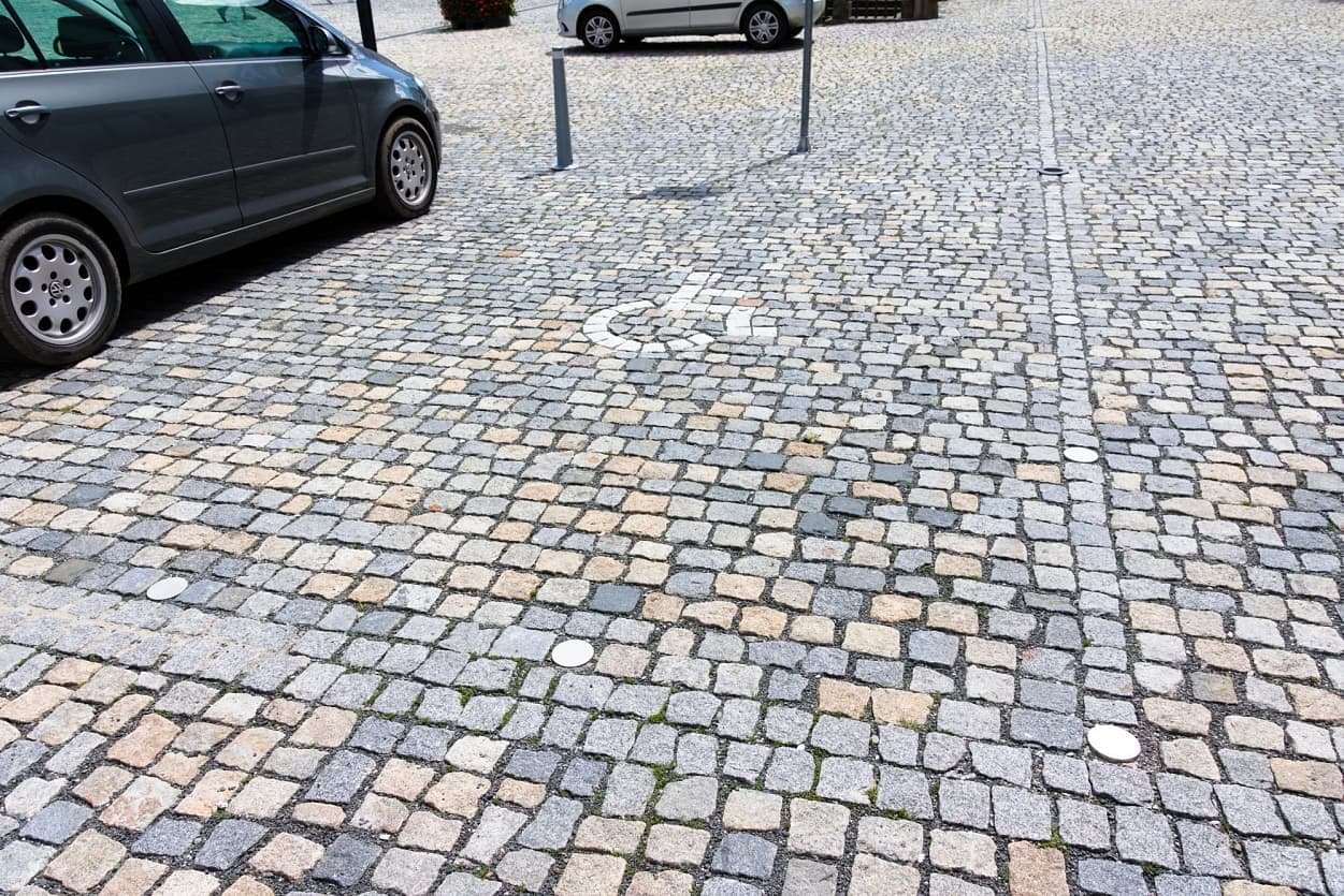 Parkovací místo pro invalidy na náměstí s dlažbou z přírodního kamene v různých odstínech.