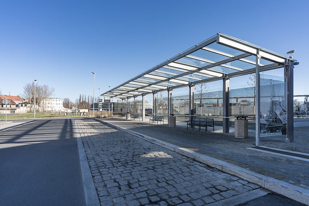 Moderní autobusový terminál v Kralupech nad Vltavou s proskleným přístřeškem, lavičkami a kombinací žulové dlažby.
