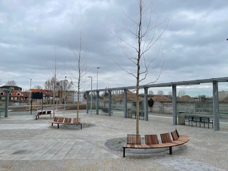 Odpočinková zóna autobusového terminálu v Kralupech nad Vltavou s moderními lavičkami, vysazenými stromy a žulovou dlažbou.