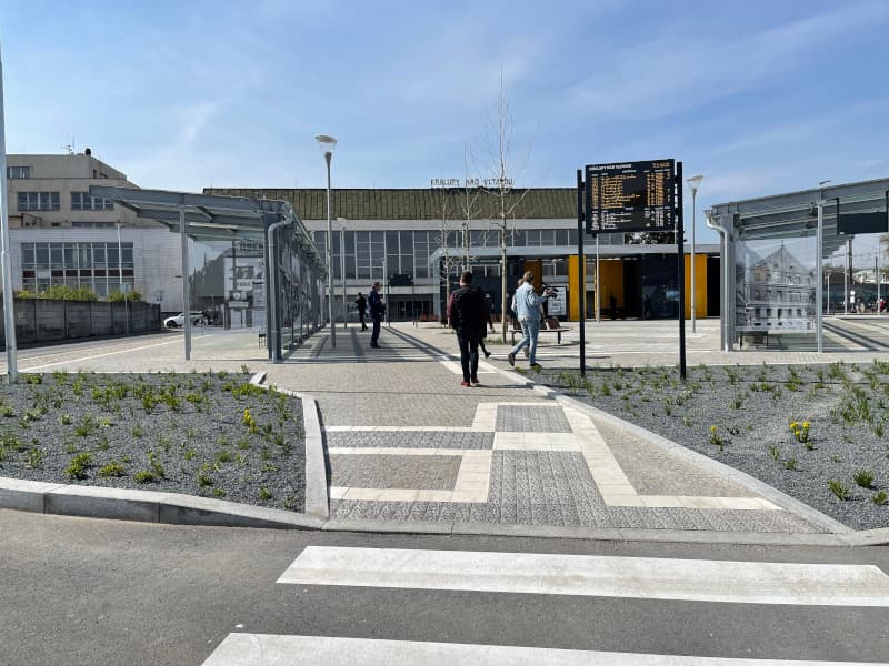 Vstup do autobusového terminálu v Kralupech nad Vltavou s informační tabulí, prosklenými přístřešky, žulou a zelení.