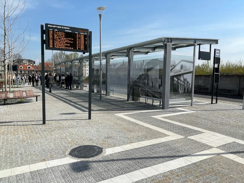 Autobusový terminál v Kralupech nad Vltavou s informační tabulí, přístřešky s historickými fotografiemi a žulovou dlažbou.