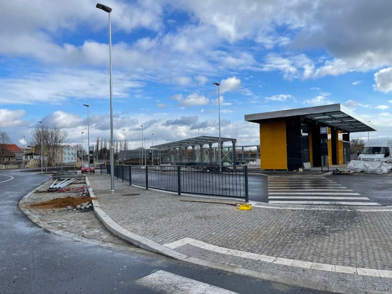 Autobusový terminál v Kralupech nad Vltavou během výstavby, s moderními přístřešky, žulovou dlažbou a veřejným osvětlením.