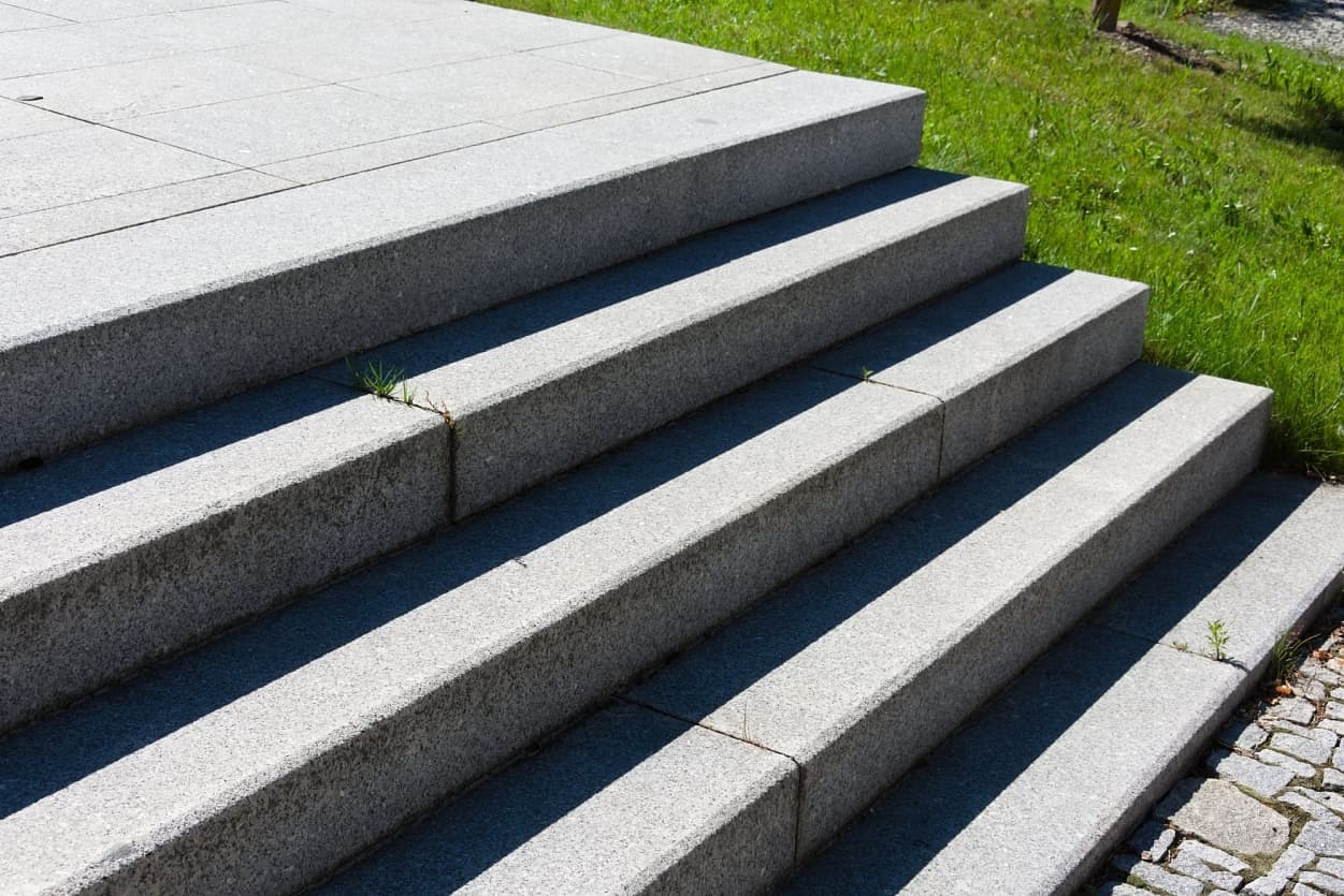 Masivní žulové schody v šedé barvě s precizním opracováním, které zajišťují odolnost a bezpečnost veřejného prostoru.