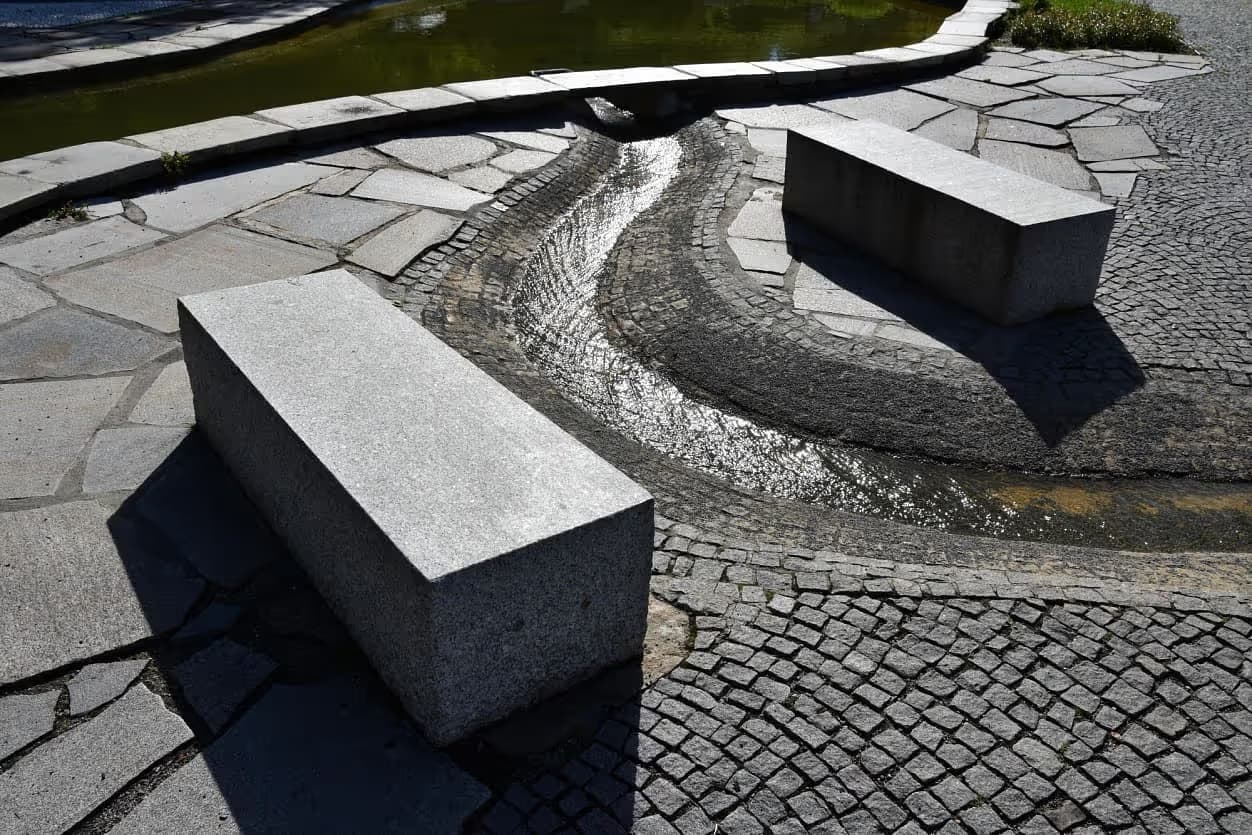 Žulové bloky sloužící jako lavičky u vodního prvku v Priessnitzových léčebných lázních, obklopené dlažbou z přírodního kamene