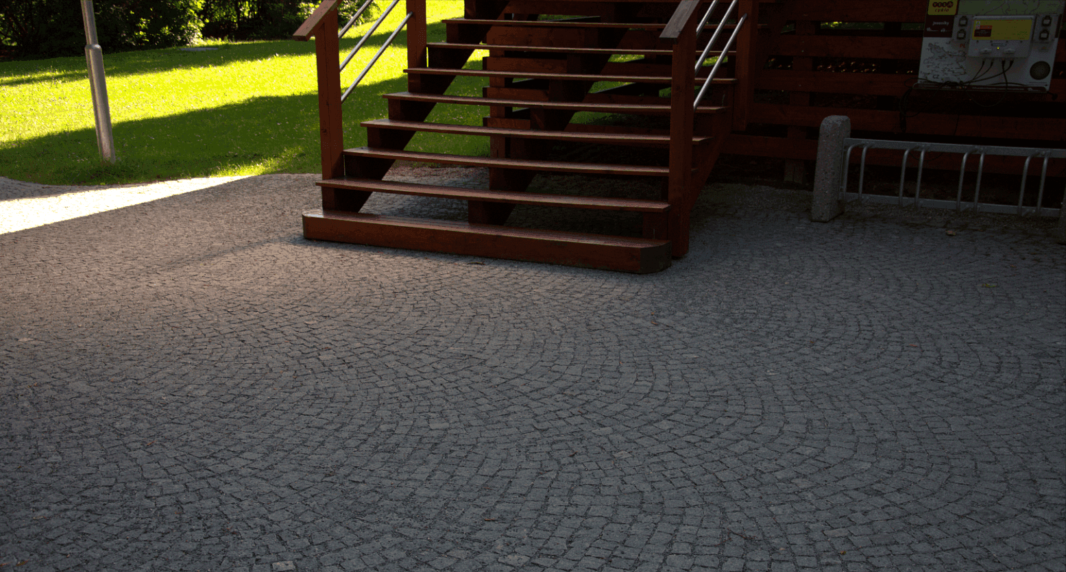 Žulová štípaná dlažba ve vějířovém vzoru u dřevěného schodiště s kovovým zábradlím, vytvářející odolný a estetický povrch.