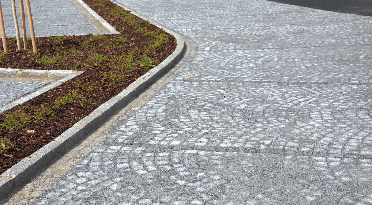 Žulová štípaná dlažba ve vějířovém vzoru s precizně osazenými obrubníky, oddělující parkovací plochu od ostrůvku s výsadbou.