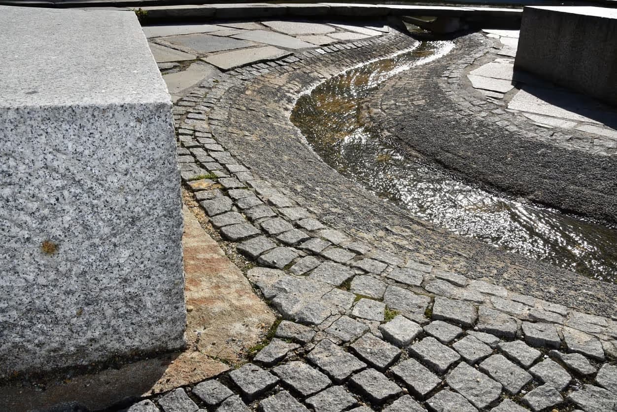 Detail žulového bloku u vodního prvku v Priessnitzových léčebných lázních, obklopeného dlažbou z přírodního kamene.