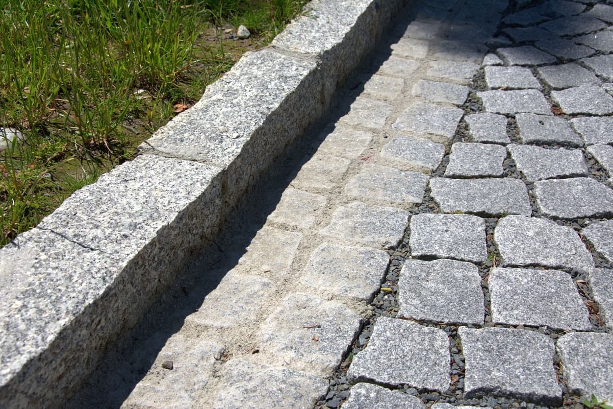 Detail žulového štípaného krajníku se žlábkem a štípanou žulovou dlažbou, která zajišťuje pevnost a odolnost povrchu.