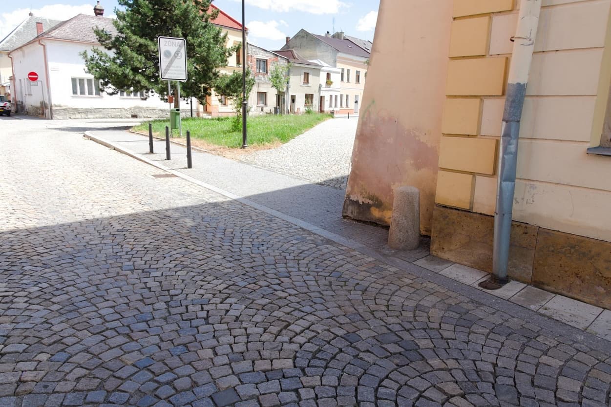 Žulová dlažba ve vějířovém vzoru, doplněná obrubníky a kamennými patníky v historické uličce Uničova.