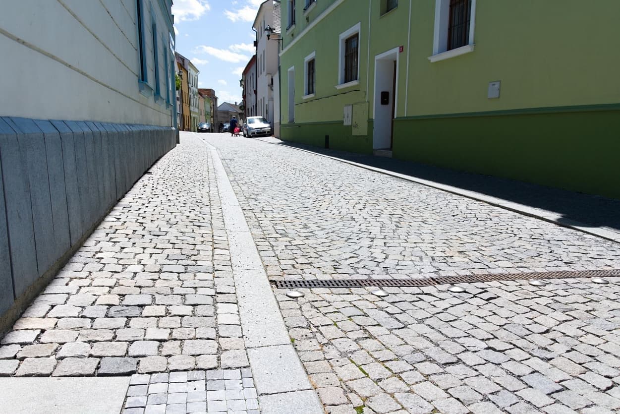 Mírně svažitá ulice v Uničově s žulovými kostkami a obrubníky, zdůrazňující historický ráz města.