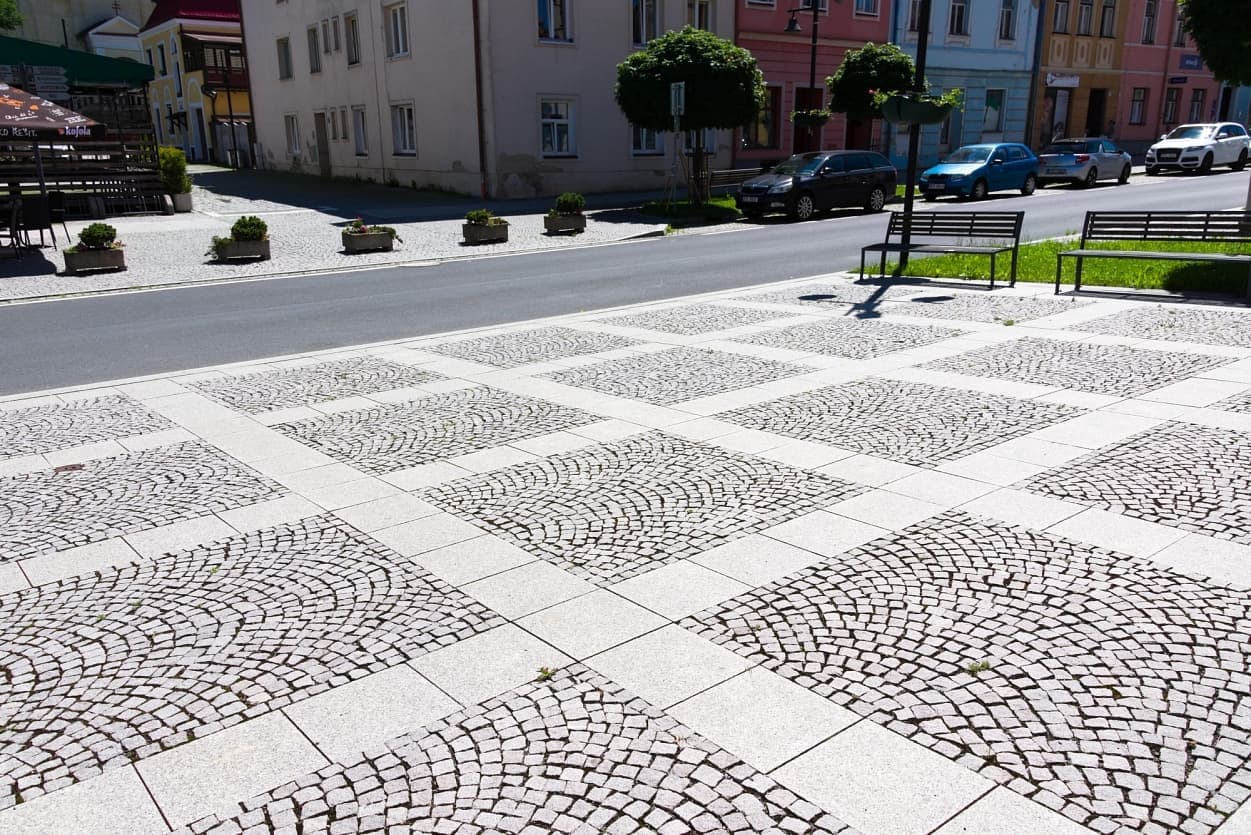 Pravidelné čtverce s vějířovou žulovou dlažbou, lemované formátovanými deskami, tvoří moderní vzor městského náměstí.