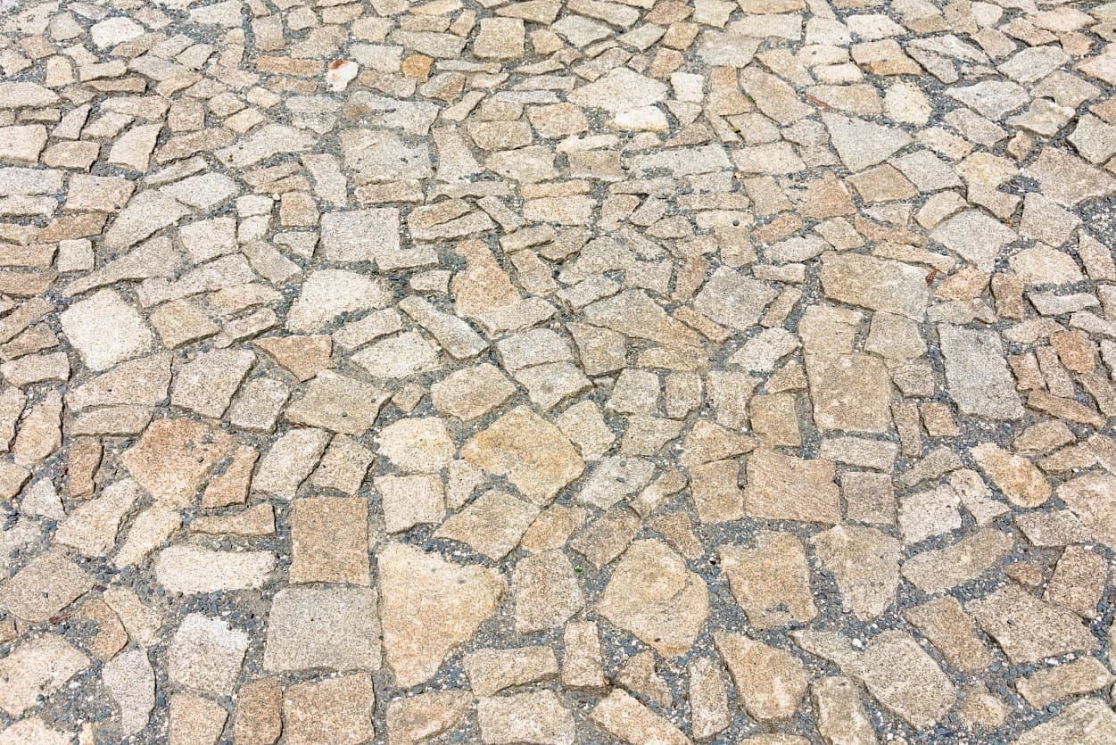 Detail dlažby z odštěpků přírodního kamene v teplých odstínech, usazené do pevného podkladu.