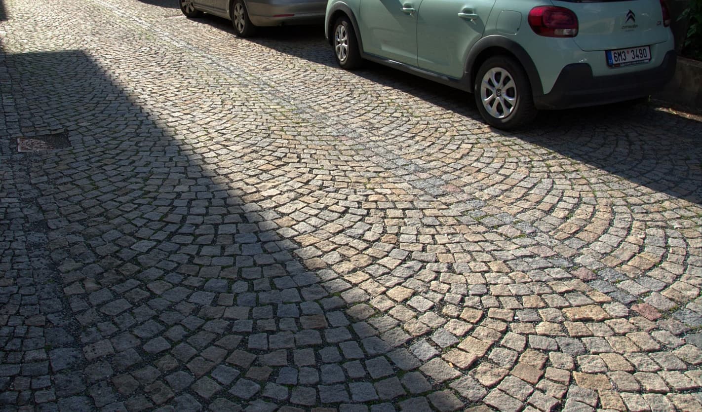 Žulová dlažba v obloukovém vzoru na ulici s parkujícími auty, kombinující šedé a žluté tóny pro estetický a trvanlivý povrch.